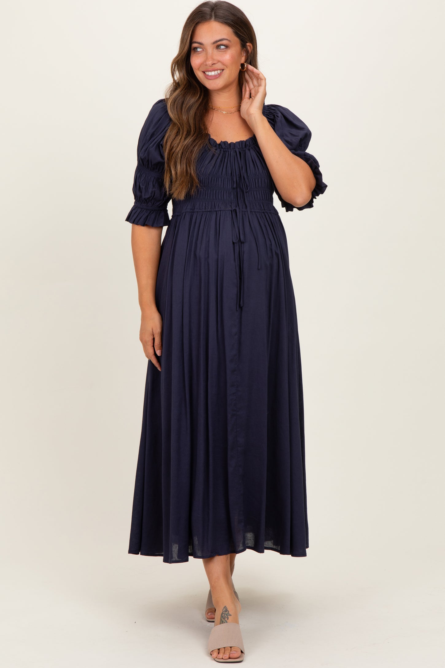 woman wearing a navy blue maternity maxi dress with puff sleeves and a smocked bodice, showing her baby bump