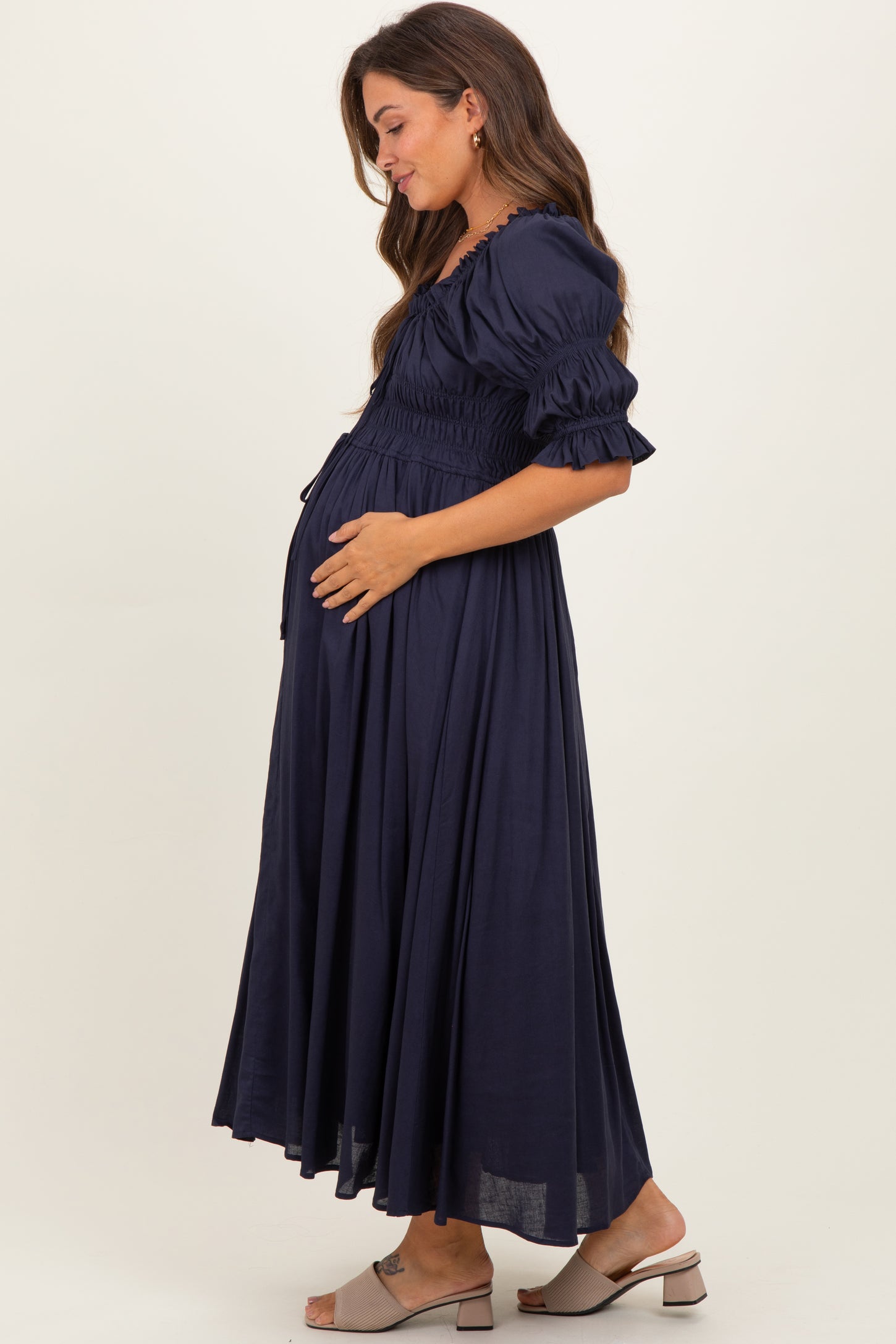 woman wearing a navy blue maternity maxi dress with puff sleeves and a gathered waist, gently holding her baby bump