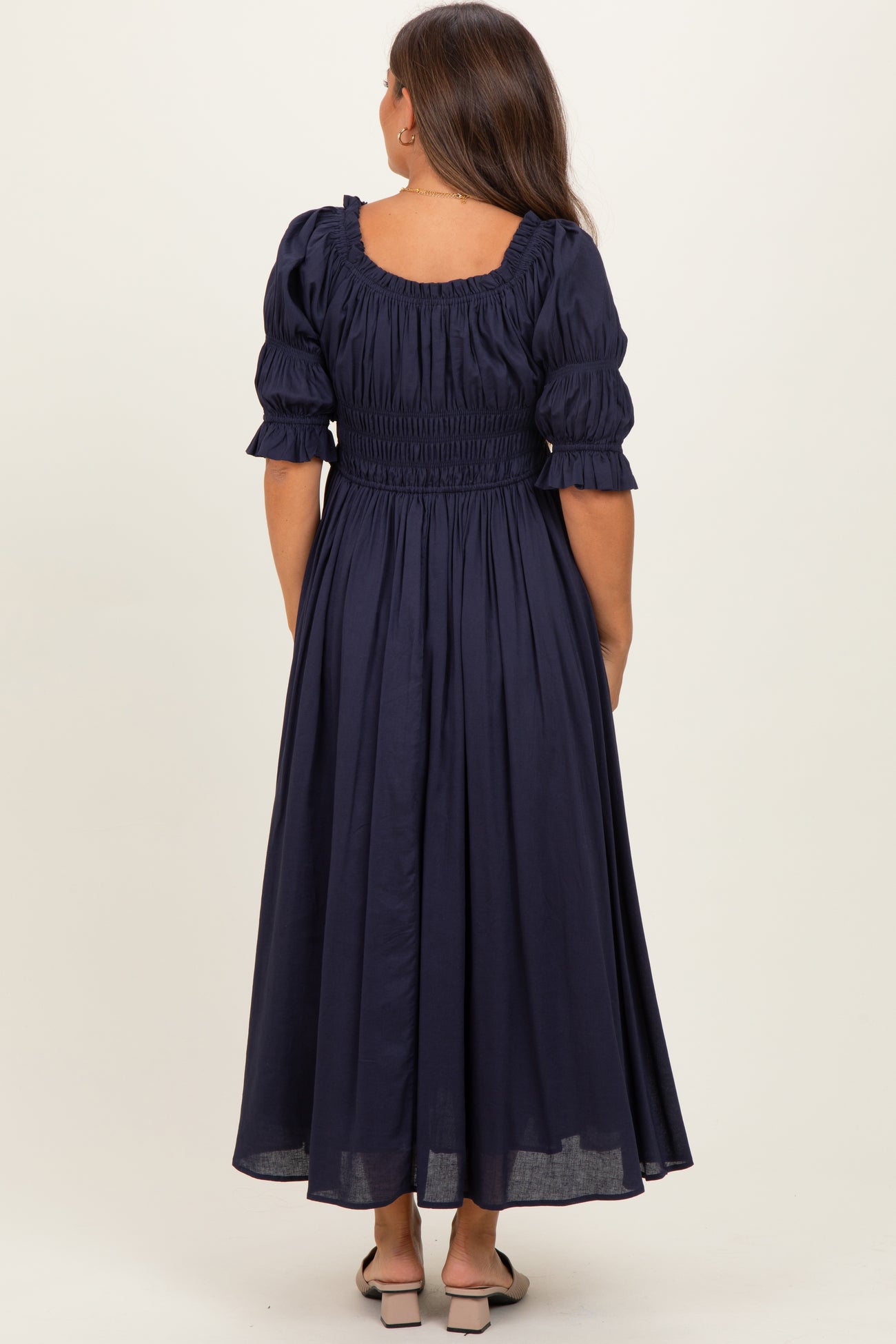 woman wearing a navy blue maternity maxi dress with a smocked bodice and puffed sleeves, seen from the back
