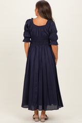 woman wearing a navy blue maternity maxi dress with a smocked bodice and puffed sleeves, seen from the back