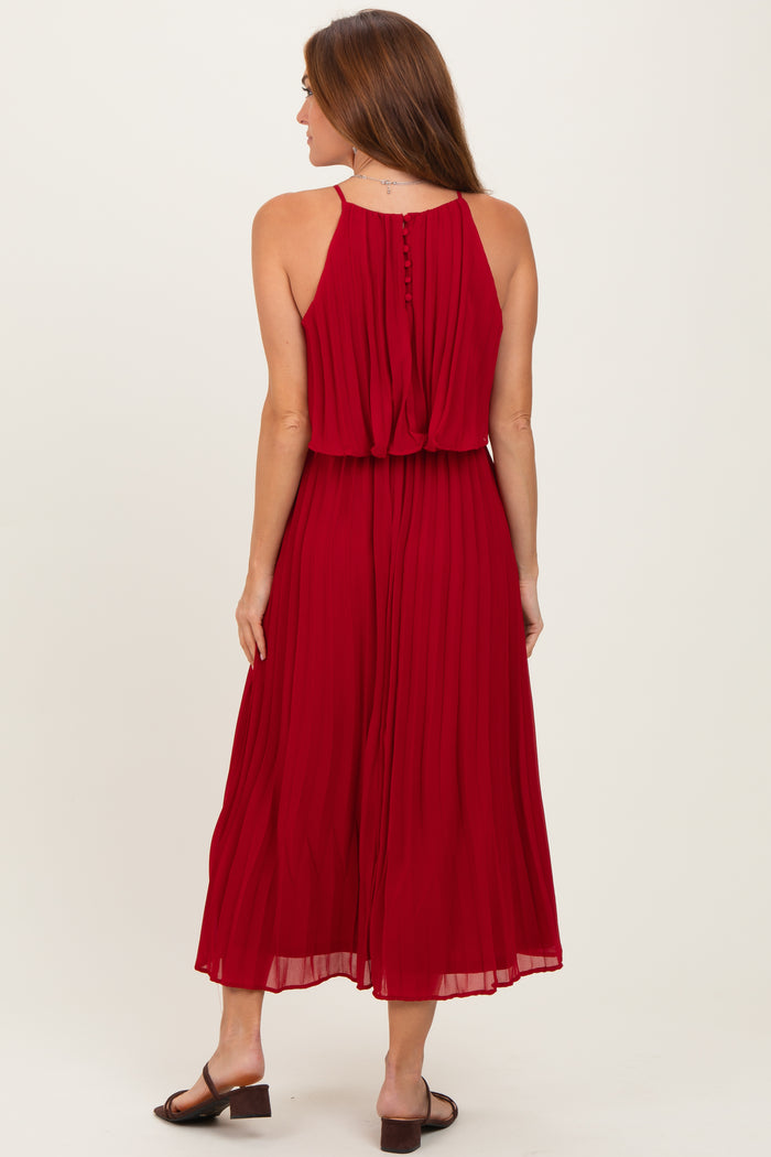 woman wearing a sleeveless red pleated maxi dress with a relaxed fit and button details at the back
