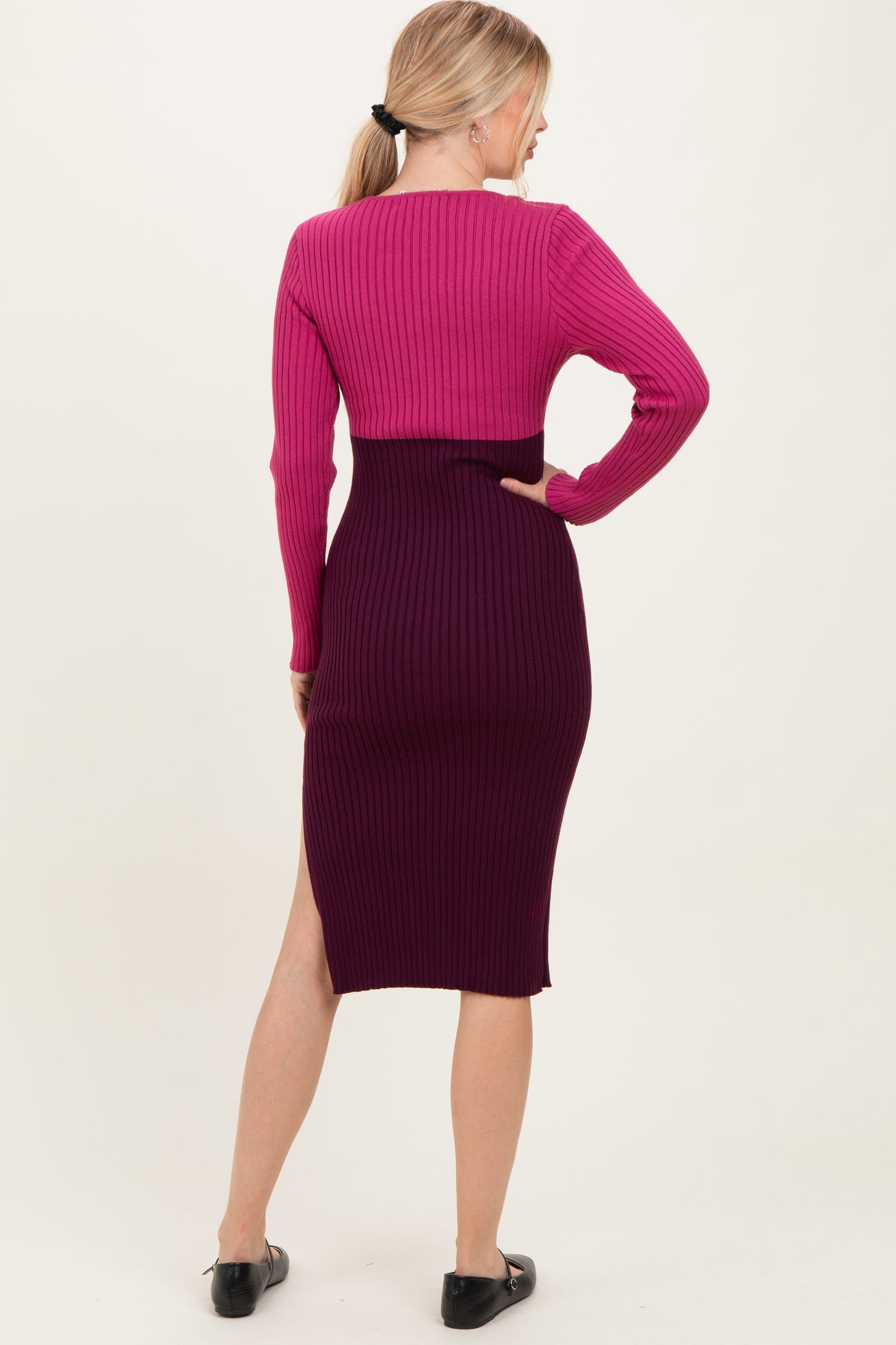 woman wearing a pink and purple ribbed midi dress with a slit at the hem and long sleeves, seen from the back