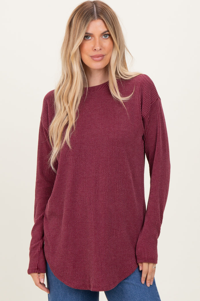 woman wearing a burgundy long sleeve ribbed top with a curved hem and relaxed fit