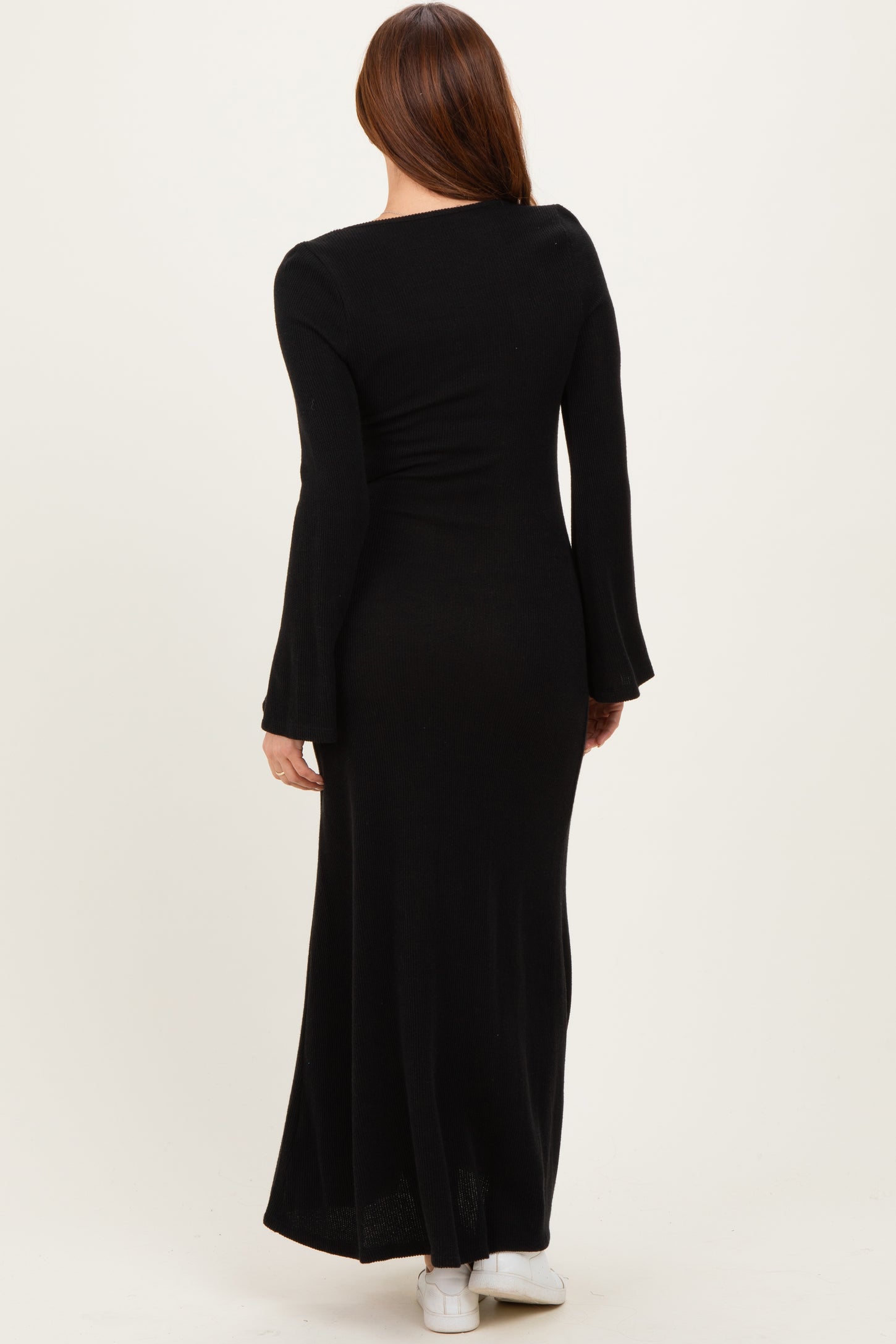 woman wearing a long black ribbed maxi dress with bell sleeves, viewed from the back