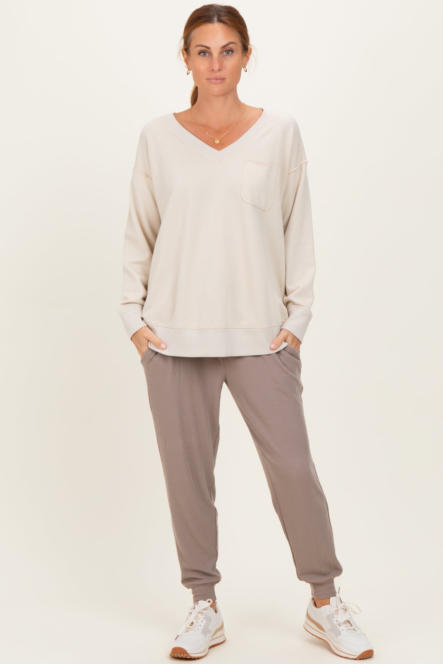 woman wearing a light beige long sleeve v-neck sweatshirt with a pocket and gray ribbed jogger pants