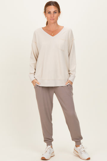 woman wearing a light beige long sleeve v-neck sweatshirt with a pocket and gray ribbed jogger pants