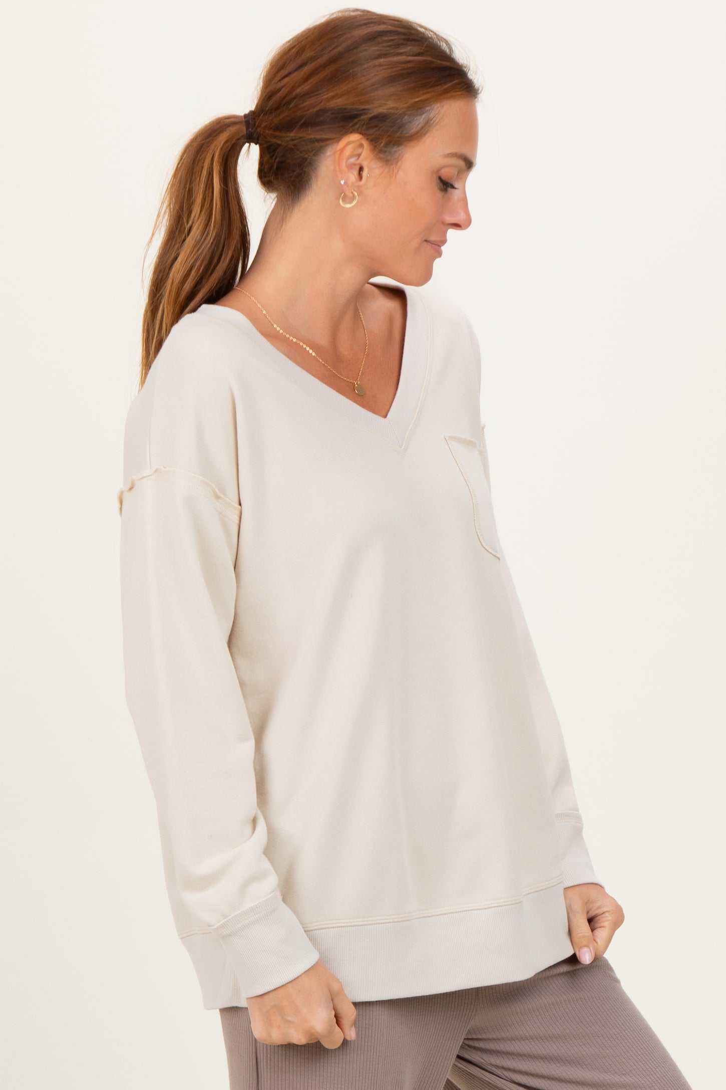woman wearing a beige long sleeve v-neck sweatshirt with a front pocket and relaxed fit