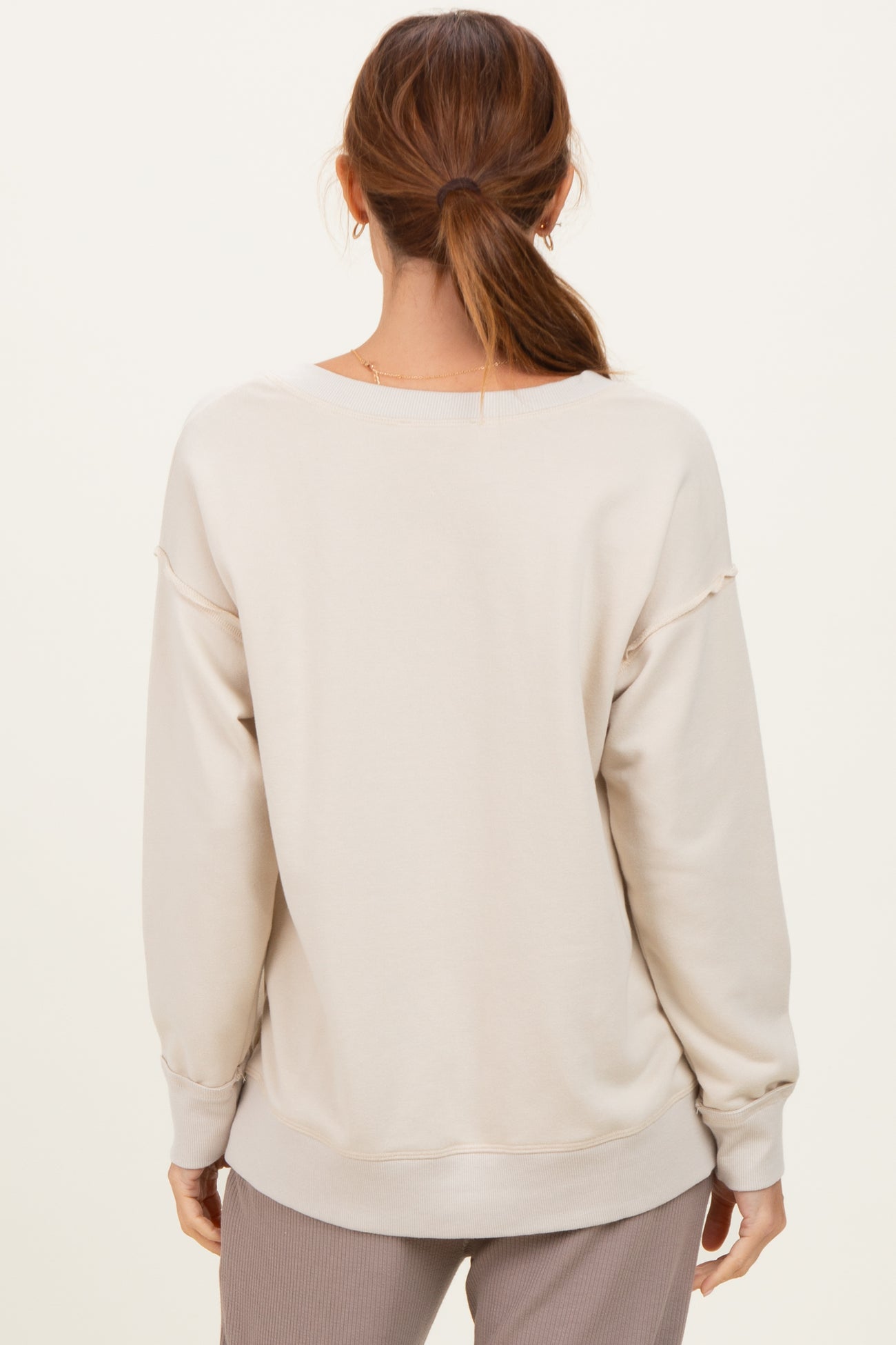 woman wearing a beige oversized sweatshirt with a relaxed fit, seen from the back