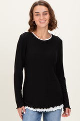 woman wearing a black long sleeve top with a white scalloped hem over a white shirt, smiling against a light background