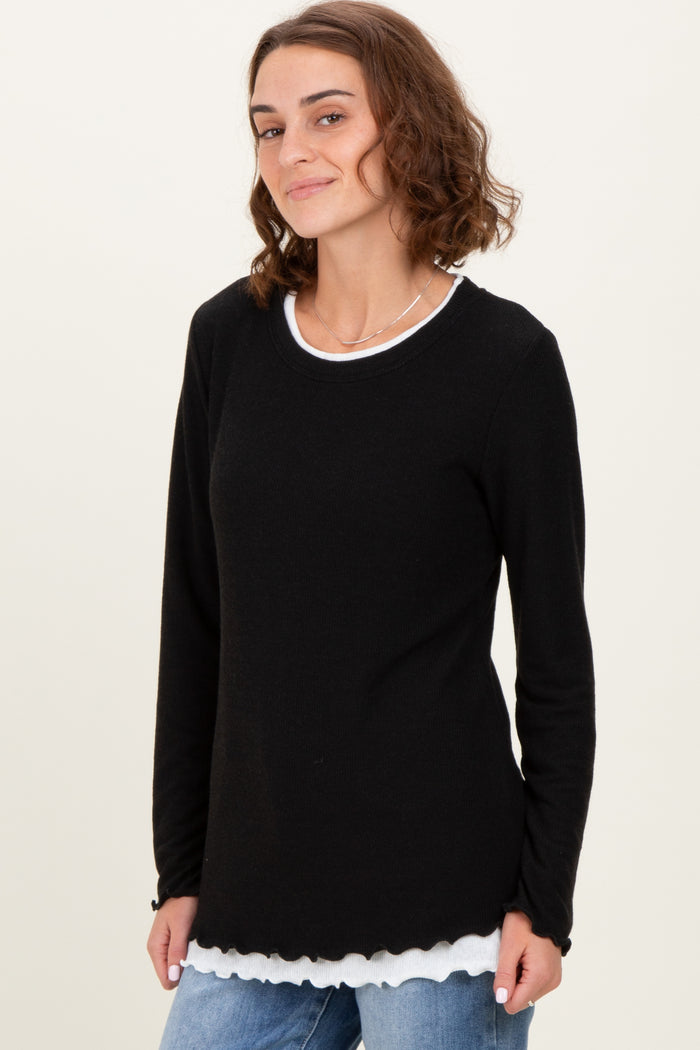 woman wearing a black long sleeve top with a scalloped hem over a white shirt, smiling at the camera