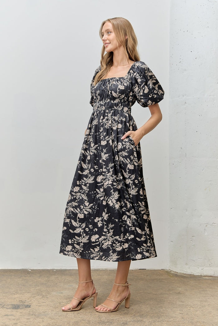 woman wearing a black floral puff sleeve midi dress with a square neckline and pockets