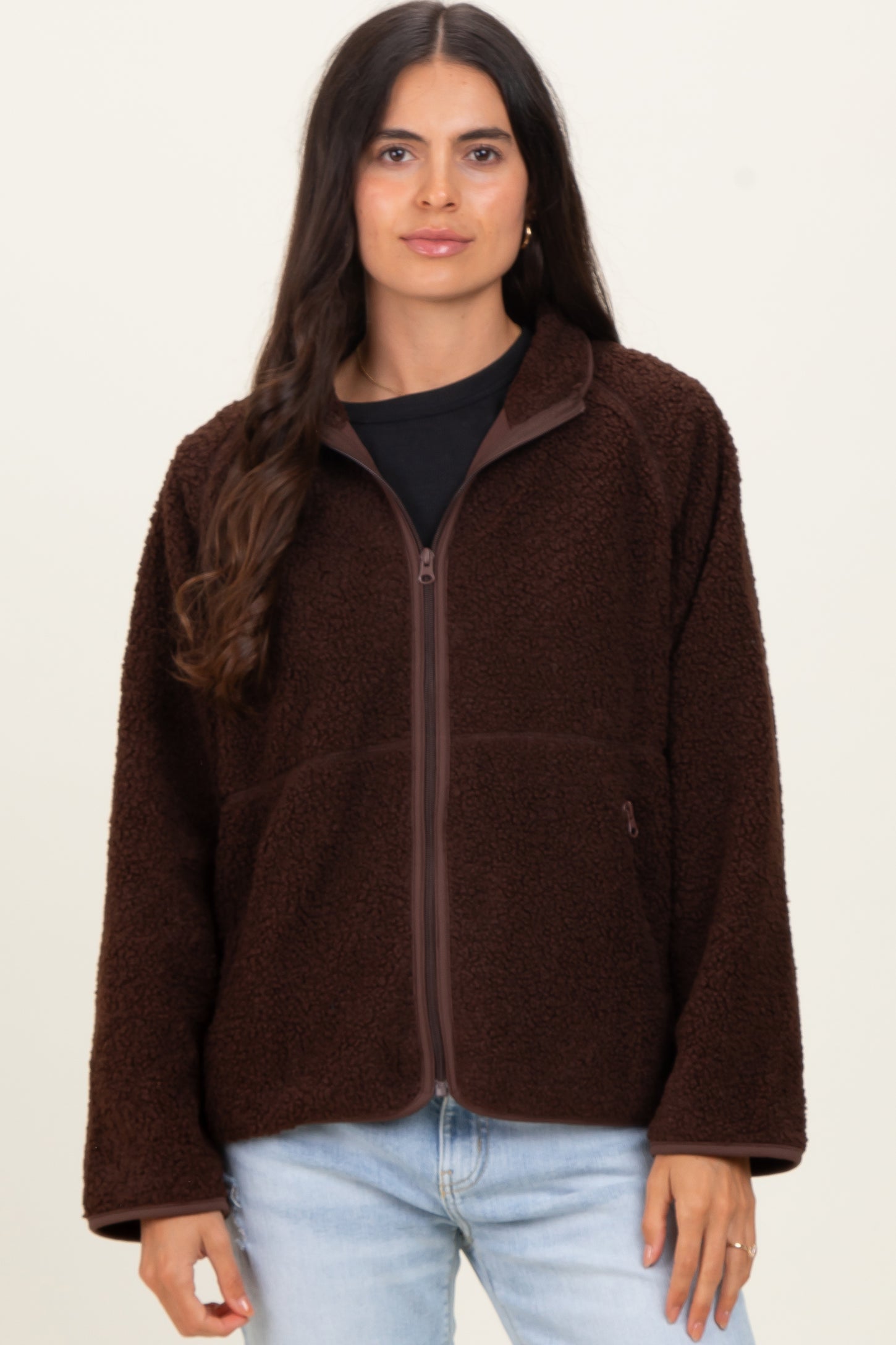 woman wearing a chocolate brown fuzzy zip-up jacket over a black top and light blue jeans