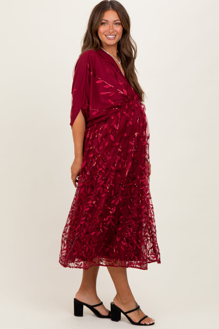 woman wearing a burgundy maternity dress with a floral lace overlay and a flowing silhouette, showcasing her baby bump