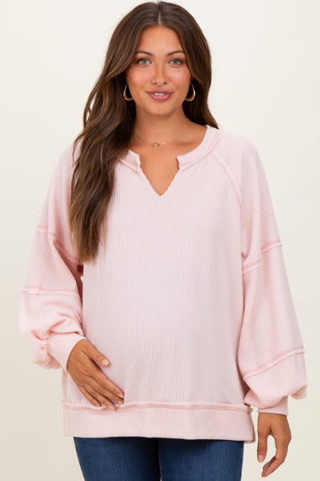 woman wearing a light pink maternity sweater with a v-neck and balloon sleeves, holding her baby bump