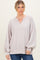 woman wearing a light beige oversized sweater with a v-neck and balloon sleeves, styled with blue jeans