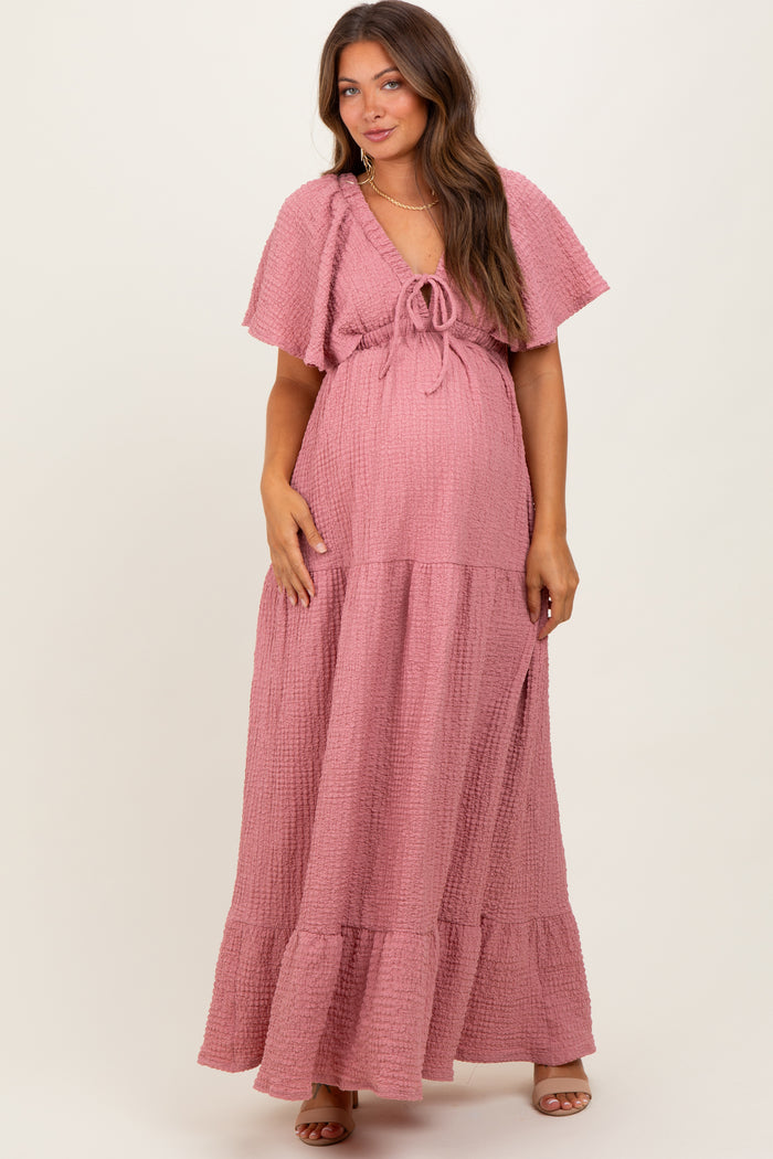 woman wearing a pink maternity maxi dress with short flutter sleeves and a tie detail at the waist, showcasing her baby bump