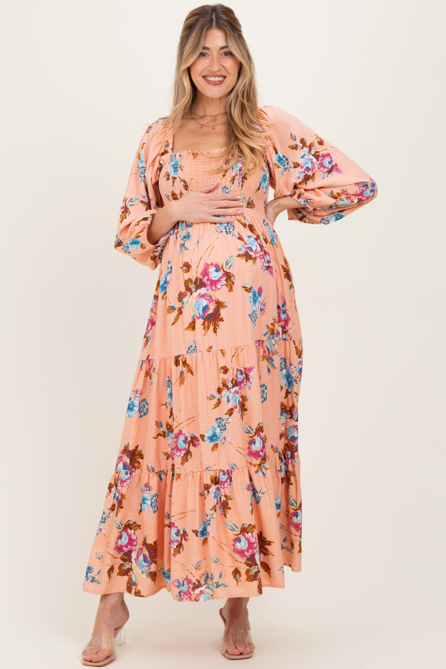 woman wearing a floral patterned pink maternity dress with long sleeves and tiered skirt, showcasing a baby bump