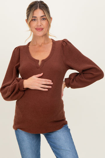 woman wearing a rust ribbed maternity top with puffed sleeves and a v-neck, holding her baby bump