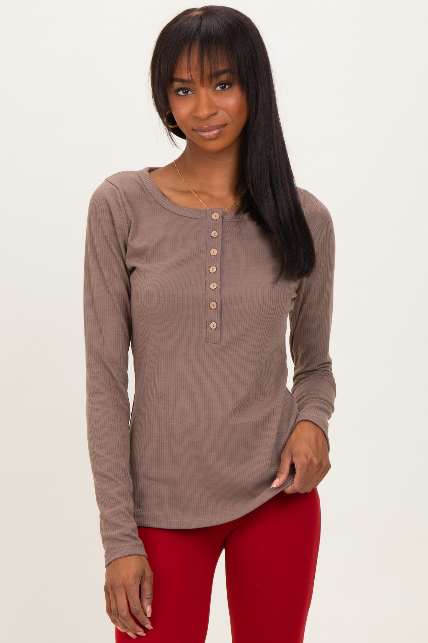 woman wearing a taupe long sleeve henley top with button details and paired with red pants