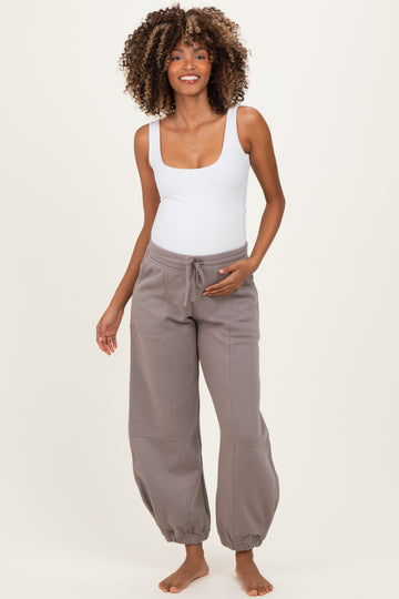 woman wearing a white scoop neck bodysuit and gray maternity joggers, showing off her baby bump