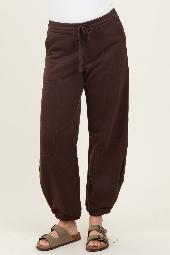 woman wearing dark brown jogger pants with an elastic waistband and gathered cuffs, paired with slide sandals