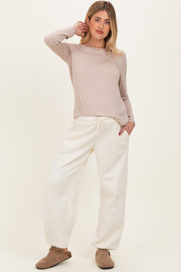 woman wearing a light beige long sleeve maternity top and cream-colored maternity jogger pants with star details