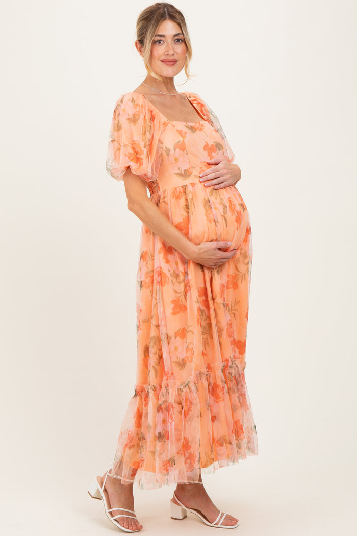 woman wearing an orange floral maternity dress with puff sleeves and a tiered skirt, cradling her baby bump