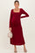 woman wearing a burgundy long sleeve maternity dress with a square neckline and gathered sides, holding a small bag