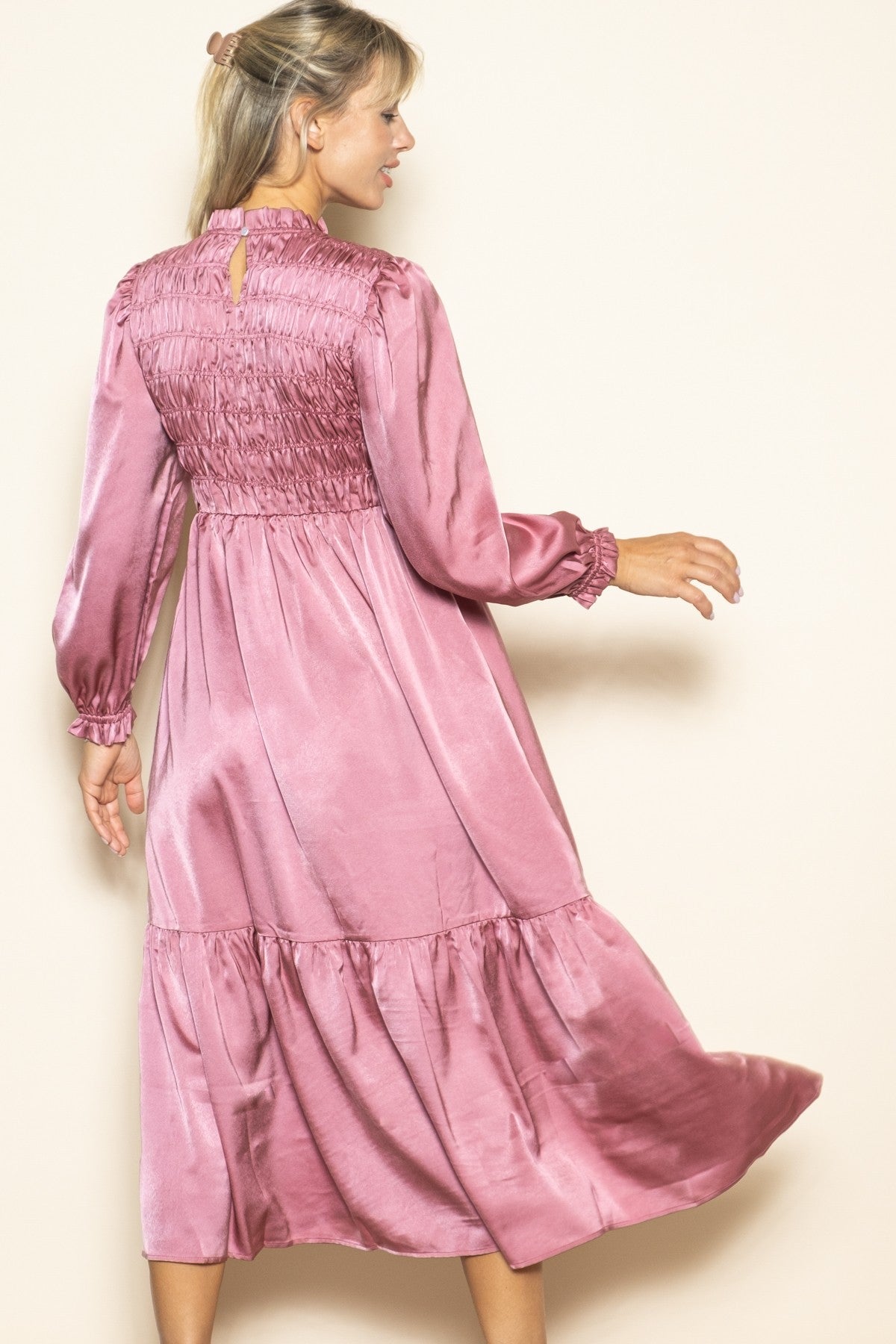 woman wearing a pink satin long sleeve dress with a smocked bodice and tiered skirt, shown from the back