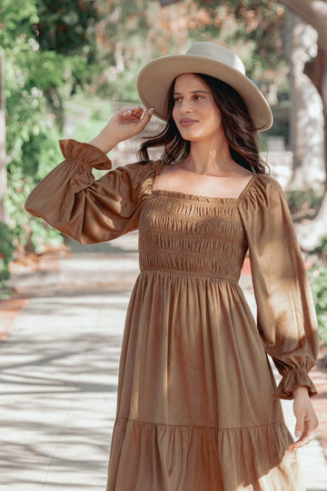 woman wearing a brown smocked maxi dress with puff sleeves and a wide-brimmed hat, posing outdoors