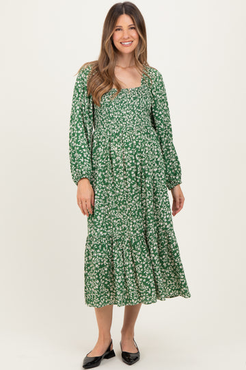 woman wearing a green floral maternity dress with long sleeves and a tiered skirt, showing her baby bump