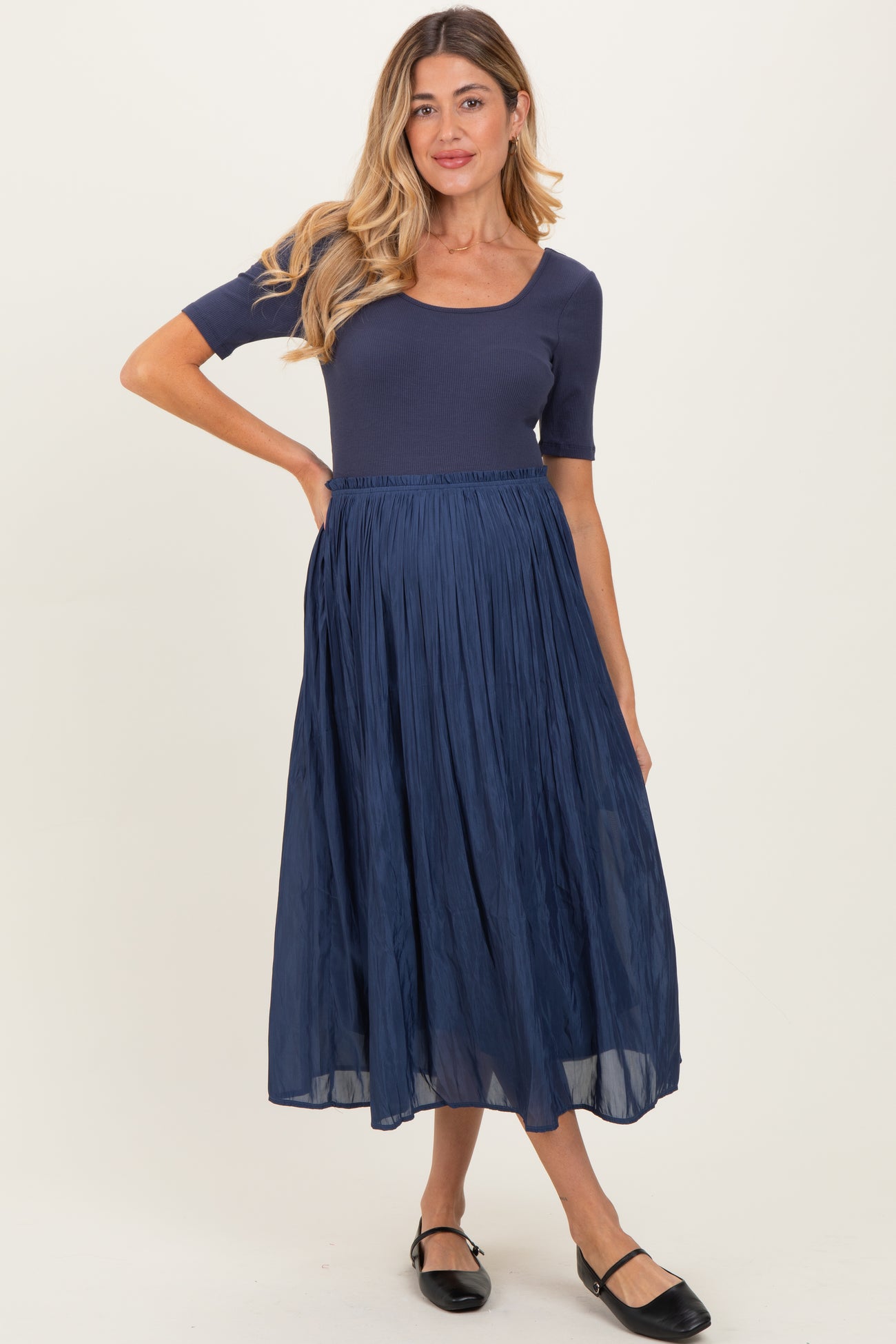 woman wearing a navy blue maternity dress with a ribbed top and a flowy pleated skirt