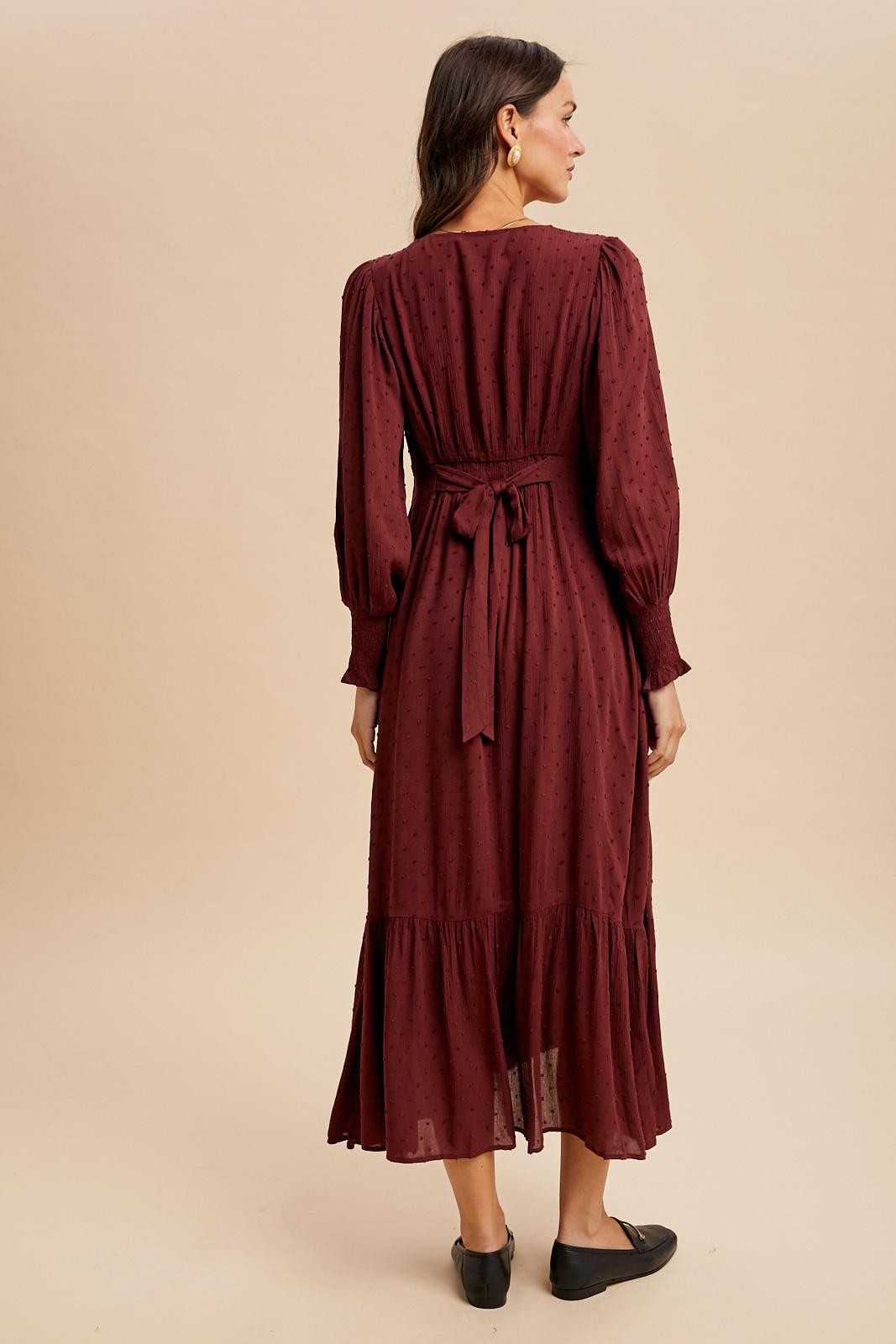 woman wearing a burgundy long sleeve dress with a tie waist and tiered hem, viewed from the back