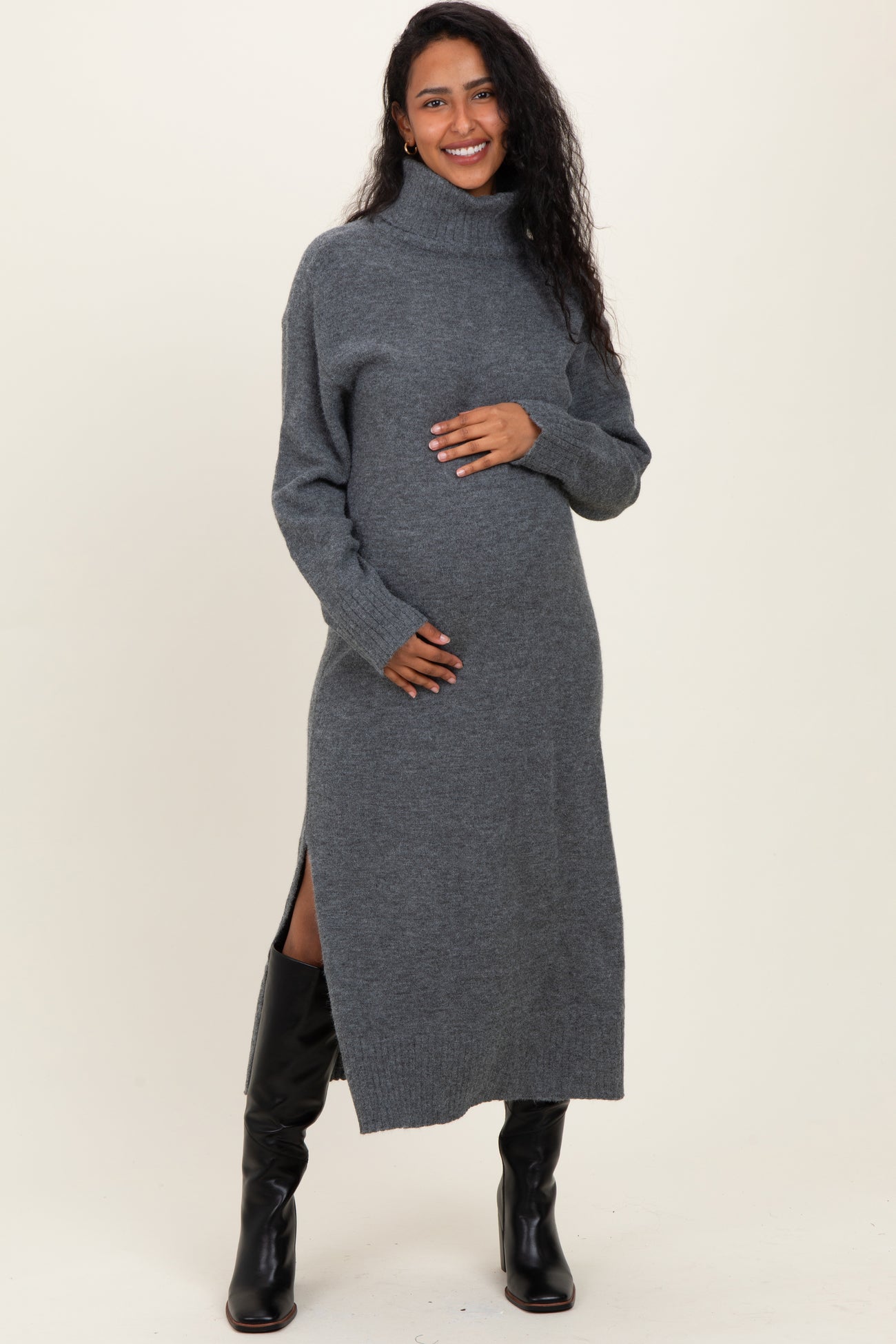 woman wearing a grey turtleneck maternity sweater dress with side slits and cradling her baby bump