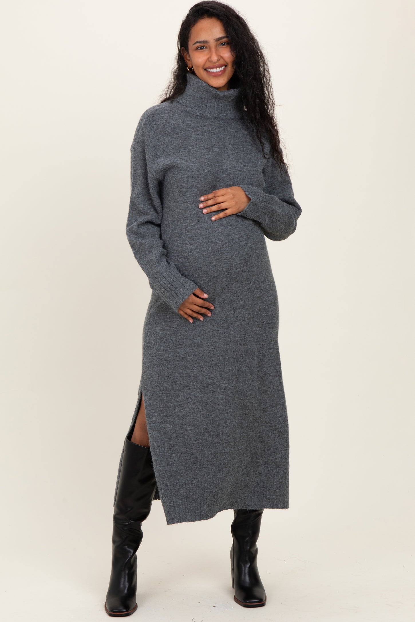 woman wearing a grey turtleneck maternity sweater dress with side slits and cradling her baby bump