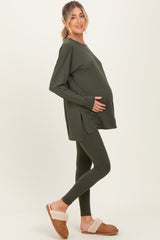 woman wearing a dark green long sleeve maternity top and matching leggings, holding her baby bump