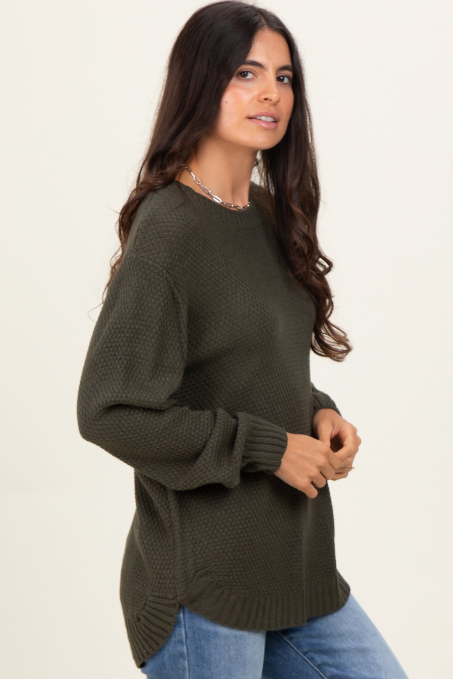 woman wearing a dark green textured long sleeve sweater paired with light blue jeans