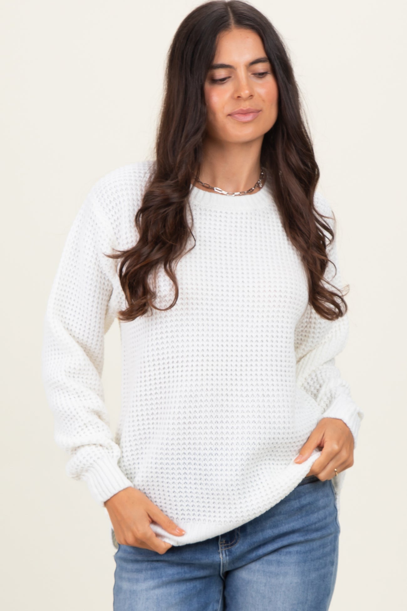 woman wearing a white waffle knit sweater with long sleeves and a relaxed fit, paired with blue jeans