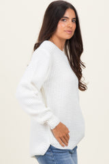 woman wearing a white waffle knit oversized sweater with long sleeves and side slits, paired with blue jeans