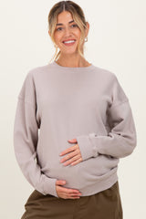 woman wearing a light brown oversized maternity sweatshirt and holding her baby bump