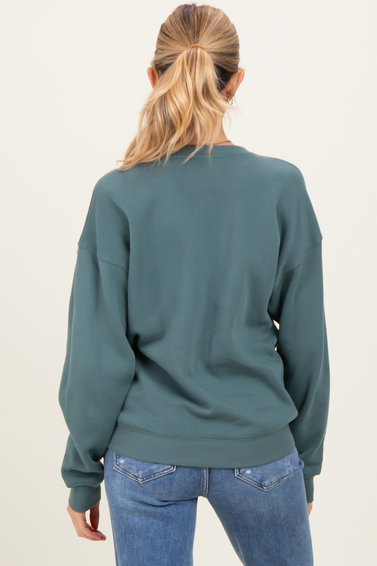 woman wearing a green maternity sweatshirt with a relaxed fit, shown from the back, paired with blue jeans