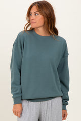woman wearing a teal oversized sweatshirt with long sleeves and ribbed cuffs, styled with gray lounge pants