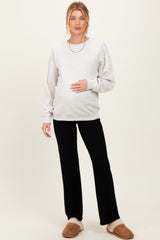 woman wearing a light gray maternity sweatshirt and black pants, holding her baby bump