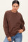 woman wearing a brown oversized sweatshirt with ribbed cuffs and a crew neckline, styled with blue jeans