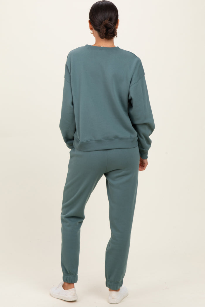 woman wearing a relaxed fit teal sweatshirt and matching joggers, standing with her back to the camera