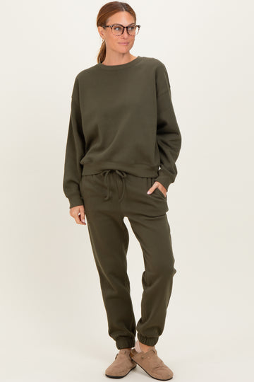 woman wearing a dark green cozy sweatshirt and matching joggers, standing with hands in pockets