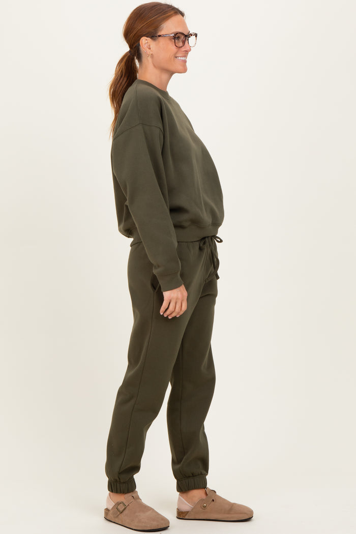 woman wearing an olive green sweatshirt and matching joggers, standing sideways and smiling