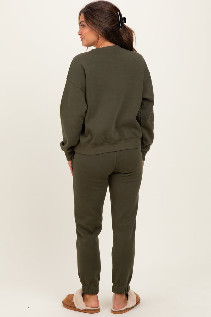 woman wearing a dark olive green maternity sweatsuit standing with back to the camera