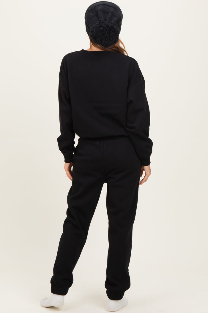 woman wearing a black oversized sweatshirt and matching sweatpants, standing with her back to the camera