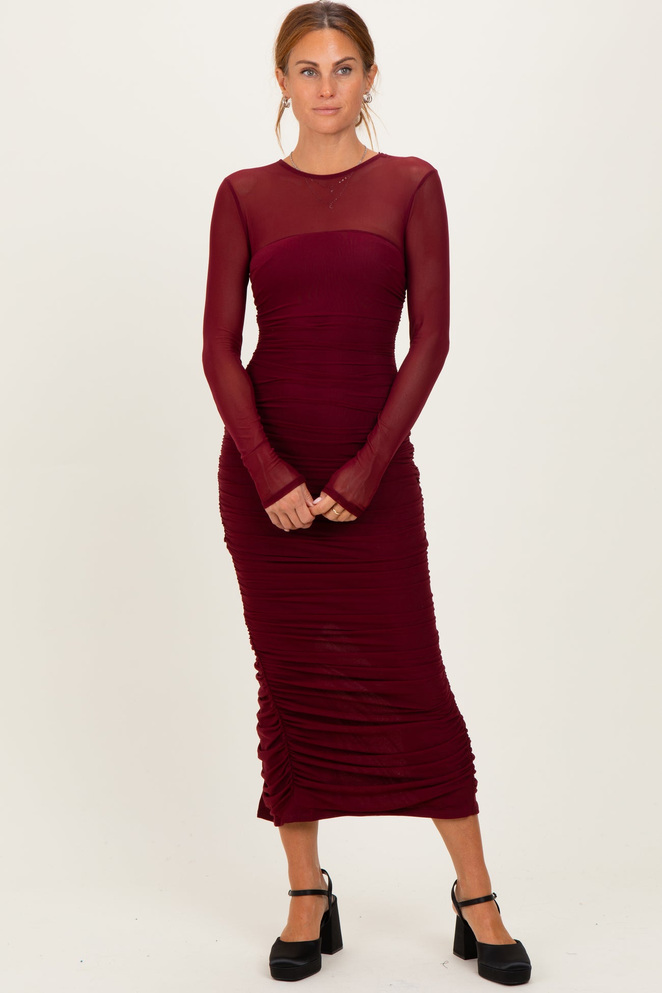 woman wearing a burgundy long sleeve midi dress with sheer neckline and ruched detailing